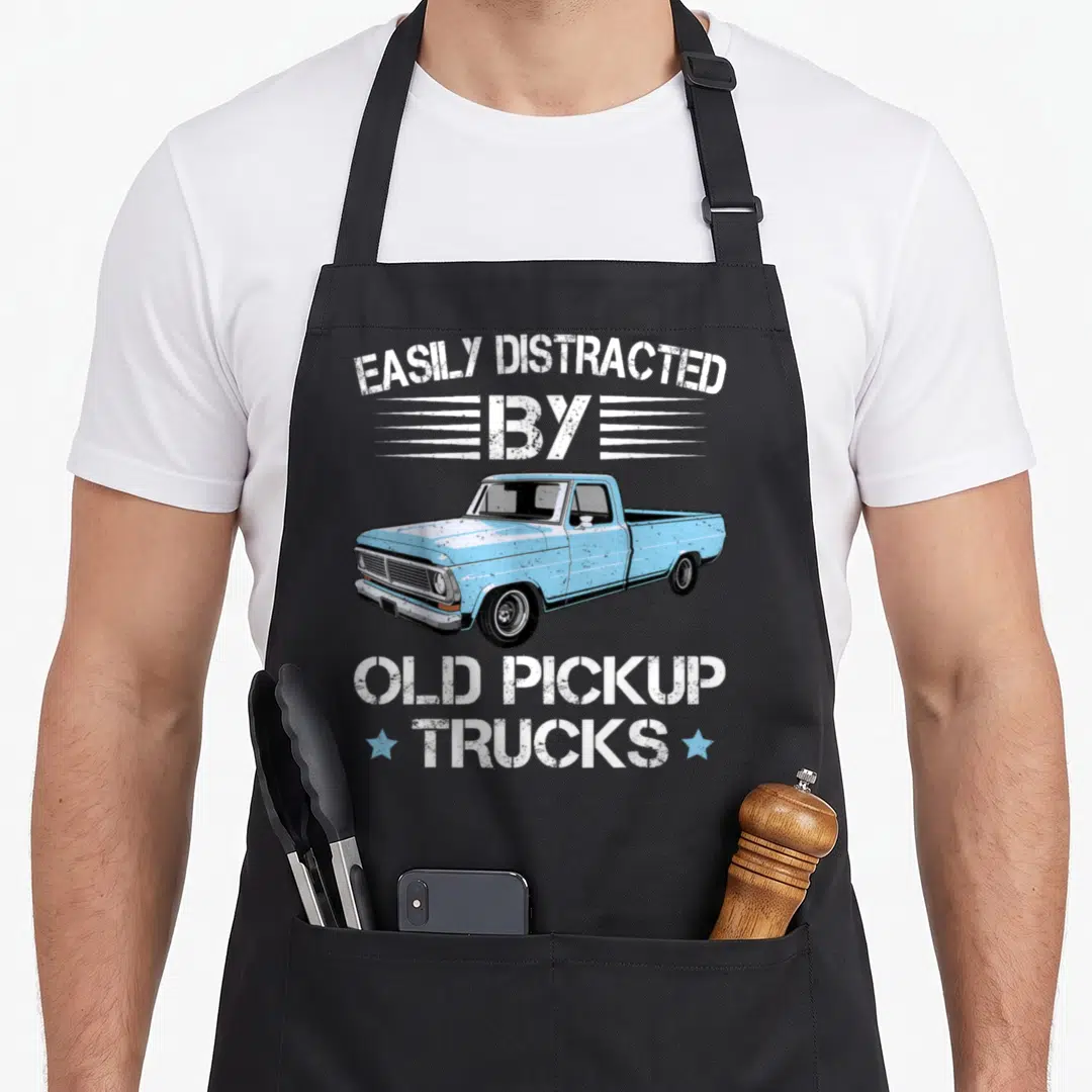 Distracted truck apron - Light blue vintage pickup truck with white distressed text and two blue stars — shown on a black cotton canvas apron against a white background