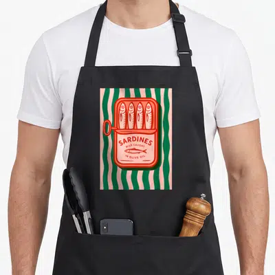 Sardine fish apron - Red sardine can with four fish and olive oil text on pink green stripes — shown on a black cotton canvas apron against a white background