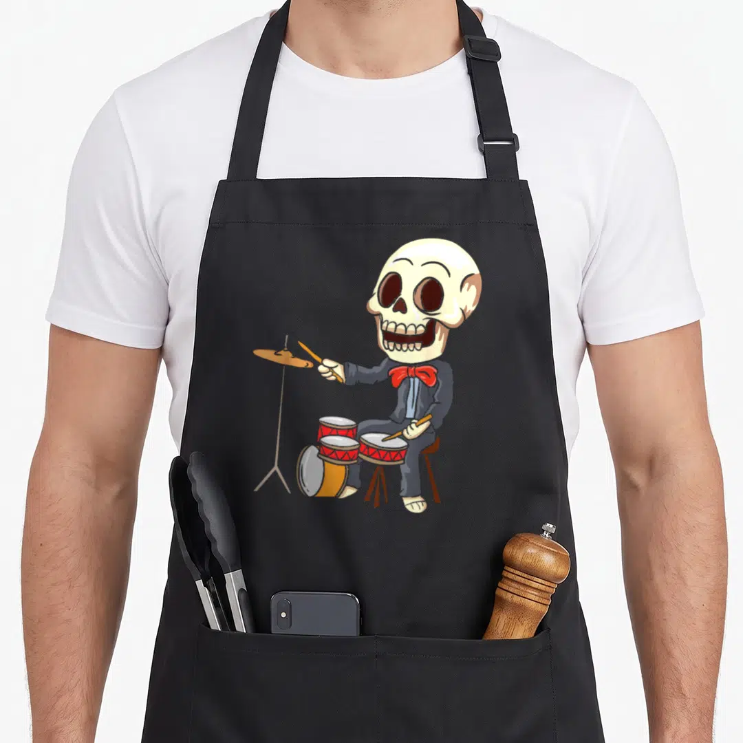 Drumming skeleton apron - Cartoon skeleton in suit playing red and gold drum kit on black apron — shown on a black cotton canvas apron against a white background