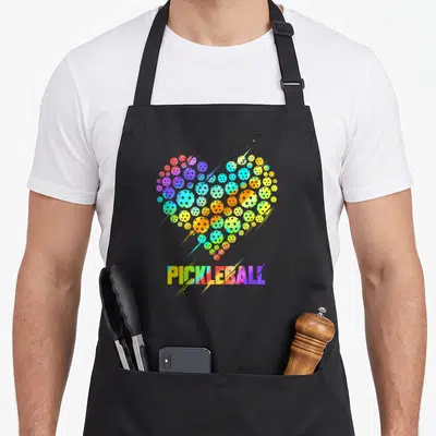 Pickleball colorful aprons - Rainbow heart of pickleballs above PICKLEBALL text — shown on a black cotton canvas apron against a white background