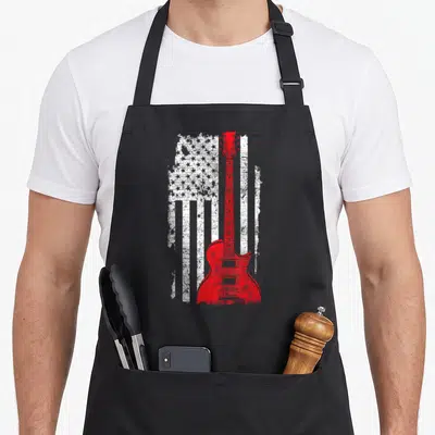 Guitarist world music apron - Red electric guitar silhouette over distressed white USA flag pattern — shown on a black cotton canvas apron against a white background