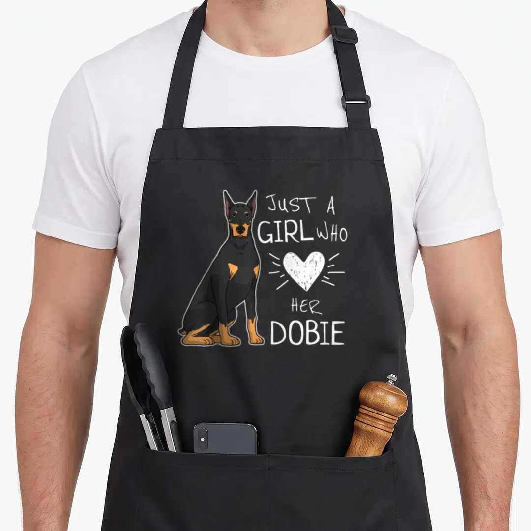 Doberman pinscher puppy dog apron - Seated cartoon Doberman next to stacked text Just A Girl Who Her Dobie and a white — shown on a black cotton canvas apron against a white background
