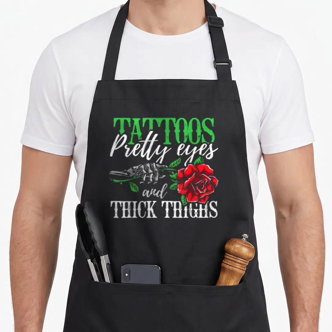 Pretty tattoo apron - Skeleton hand holding red rose with text TATTOOS Pretty eyes and THICK THIGHS — shown on a black cotton canvas apron against a white background