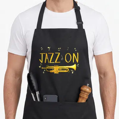 Player jazz apron - Yellow trumpet illustration below JAZZ ON text with scattered musical notes — shown on a black cotton canvas apron against a white background