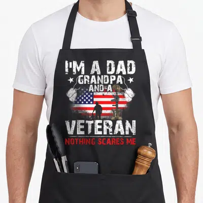 Veteran grandpa father day apron - Distressed USA flag with soldier silhouette, boots, rifle, helmet, and dog tags — shown on a black cotton canvas apron against a white background