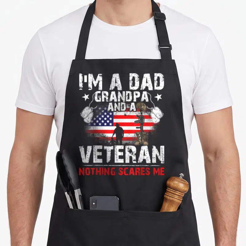 Veteran grandpa father day apron - Distressed USA flag with soldier silhouette, boots, rifle, helmet, and dog tags — shown on a black cotton canvas apron against a white background
