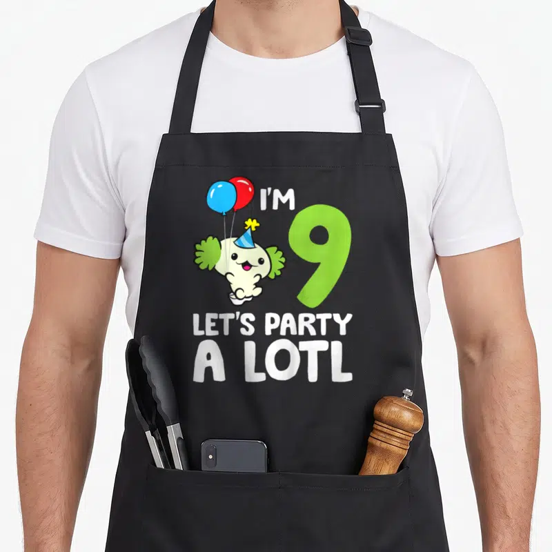 9th lotl birthday apron - Cartoon axolotl holding balloons next to green number 9 and party text — shown on a black cotton canvas apron against a white background