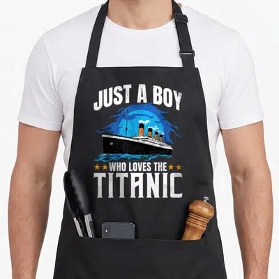 Rms novelty apron - Retro Titanic ship print with white text JUST A BOY WHO LOVES THE TITANIC and four orange stars — shown on a black cotton canvas apron against a white background
