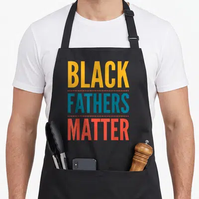 Father business apron - Stacked text reading Black Fathers Matter in yellow blue and red separated by rows of dots — shown on a black cotton canvas apron against a white background