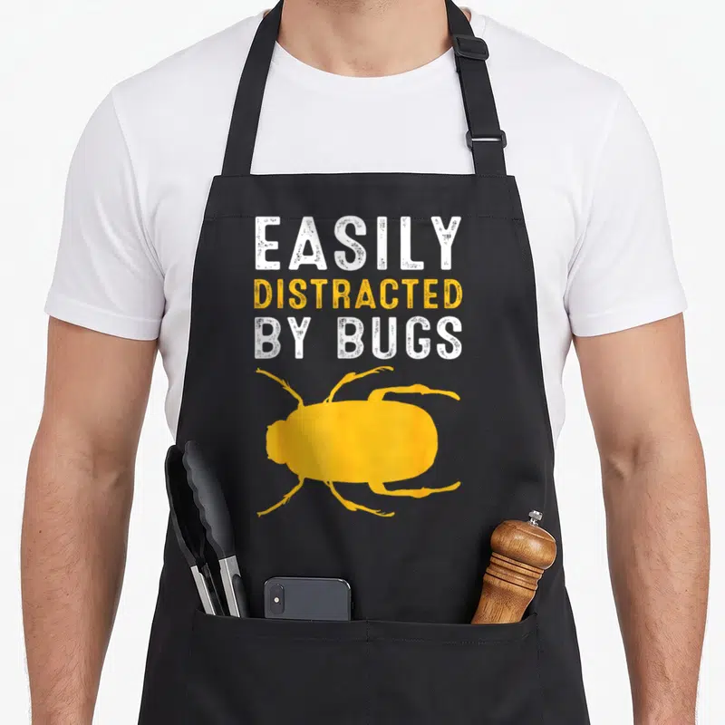 Bug insect entomologist apron - EASILY DISTRACTED BY BUGS text above yellow beetle silhouette in distressed style — shown on a black cotton canvas apron against a white background