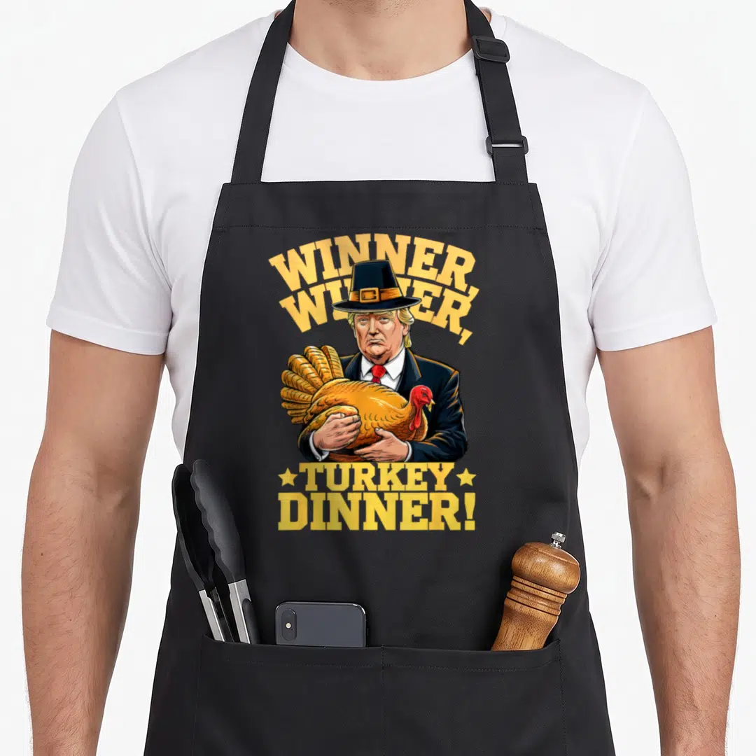 Meilan thanksgiving apron - Cartoon man in pilgrim hat holding turkey under yellow Winner Winner Turkey Dinner text — shown on a black cotton canvas apron against a white background