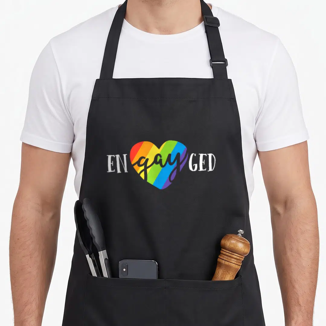Engayged bridesmaid aprons - Rainbow heart with white ENgayGED text and gray cursive overlay — shown on a black cotton canvas apron against a white background