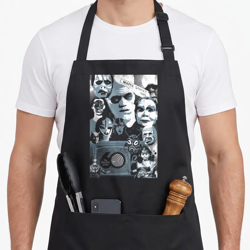 Zone dusk apron - Blue-grey collage of faces, MAPLE STREET sign, TV, doll, astronaut — shown on a black cotton canvas apron against a white background