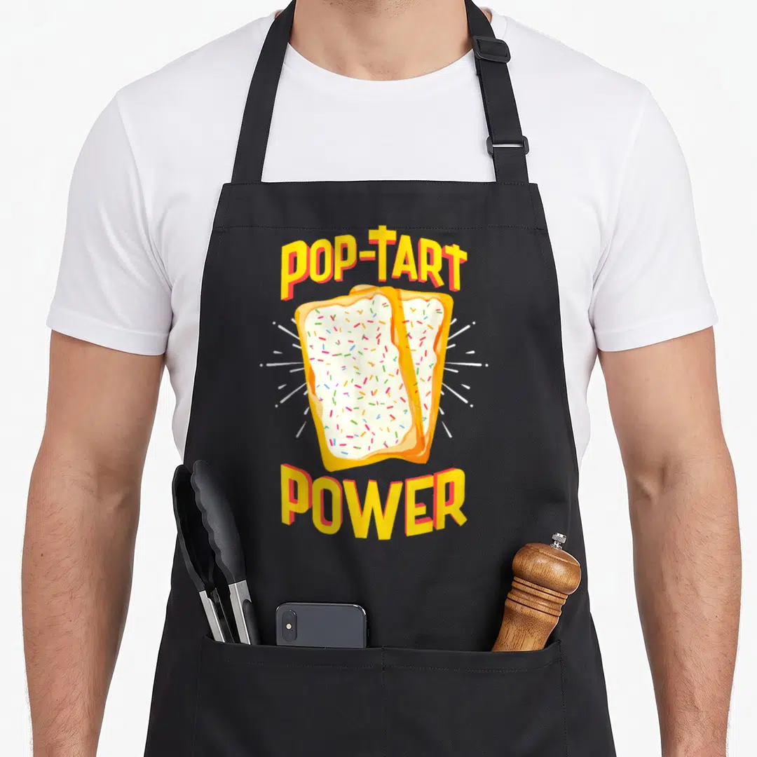 Pop tart apron - POP-TART POWER text above two frosted pastries with white rays in yellow orange white — shown on a black cotton canvas apron against a white background