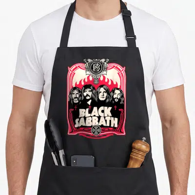Crest black sabbath apron - Four band members in red beige frame with BLACK SABBATH text and flames — shown on a black cotton canvas apron against a white background