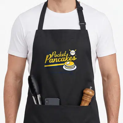 Pat milwaukee apron - Yellow and navy typography reading Pat's Pocket Pancakes above a stack of pancakes and a crossed — shown on a black cotton canvas apron against a white background