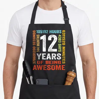Month 12th birthday apron - White number 12 surrounded by orange yellow green blue time stats and years of being — shown on a black cotton canvas apron against a white background
