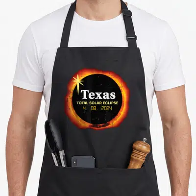 April texas apron - Texas total solar eclipse 4. 08. 2024 black circle orange corona yellow star — shown on a black cotton canvas apron against a white background