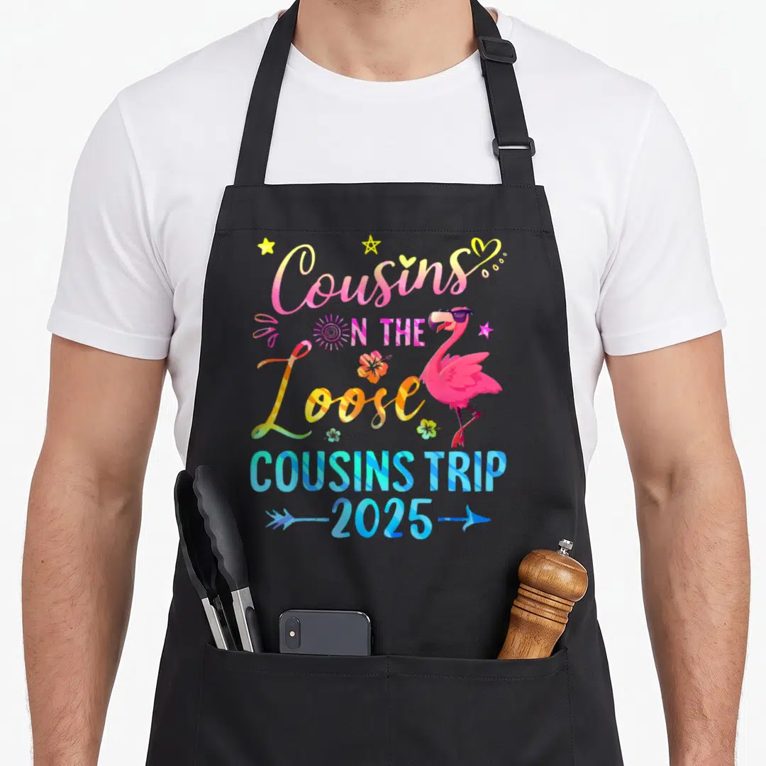 Cousin best friends family apron - Pink flamingo with sunglasses and Cousins On The Loose 2025 text surrounded — shown on a black cotton canvas apron against a white background