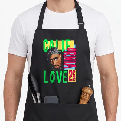 Funny california tupac apron - Tupac portrait with vertical CALIFORNIA LOVE 2PAC text in green pink yellow blue — shown on a black cotton canvas apron against a white background