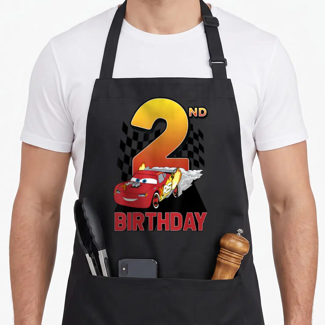 Car 2nd apron - Red cartoon race car speeding past yellow number 2 with checkered flags and birthday text — shown on a black cotton canvas apron against a white background