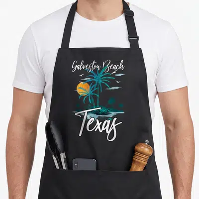Family texas apron - Retro Galveston Beach Texas print with teal palms orange sun and white script lettering — shown on a black cotton canvas apron against a white background