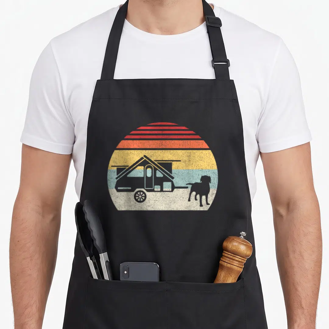 Frame dog apron - grey camper and dog silhouette against red orange yellow blue grey striped sun — shown on a black cotton canvas apron against a white background