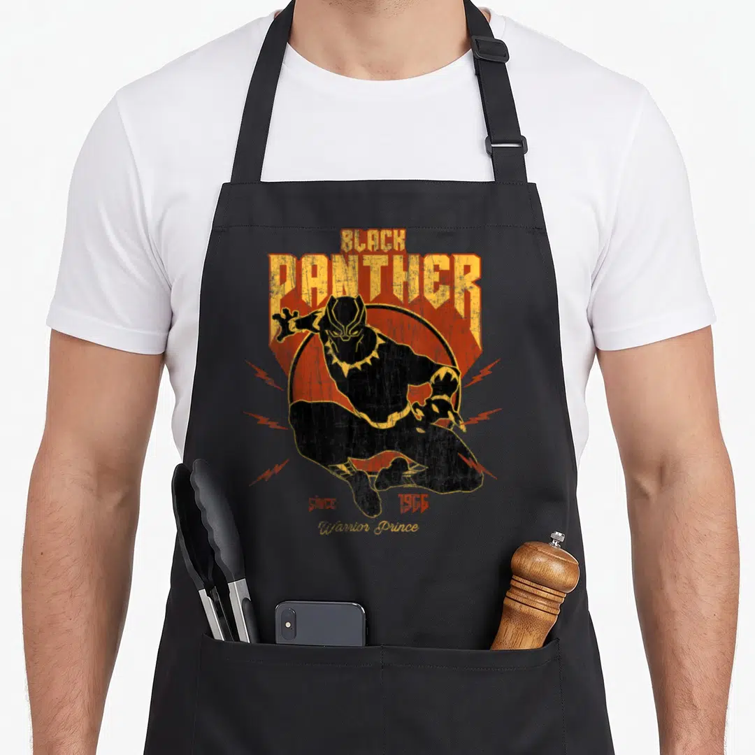 Action panther apron - Retro Black Panther leaping before orange circle with lightning bolts and text since 1966 — shown on a black cotton canvas apron against a white background