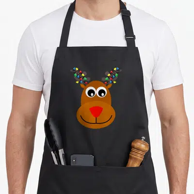 Reindeer santa red christmas apron - Cartoon reindeer head with red nose and multicolored lights wrapped around antlers — shown on a black cotton canvas apron against a white background