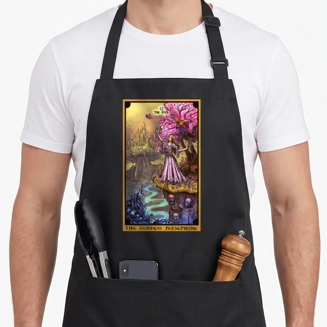 Underworld witch apron - Tarot card print with woman, gold border, pink tree, and skulls labeled The Fool The Goddess — shown on a black cotton canvas apron against a white background