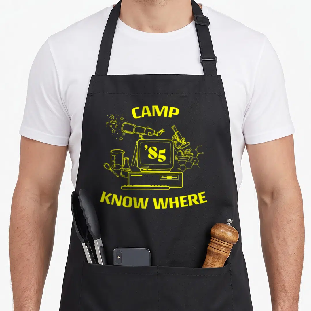 Camp novelty apron - Yellow line art of science equipment and text CAMP KNOW WHERE 85 — shown on a black cotton canvas apron against a white background