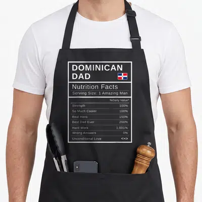 Dominican father day apron - Grey nutrition facts label showing 100% strength and infinite unconditional love — shown on a black cotton canvas apron against a white background