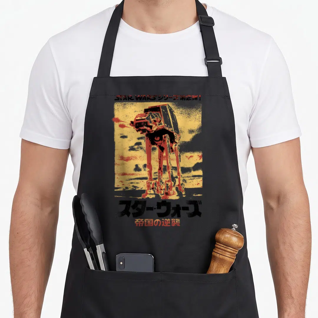 Empire japanese apron - AT-AT walker illustration on yellow background with Japanese Star Wars text — shown on a black cotton canvas apron against a white background