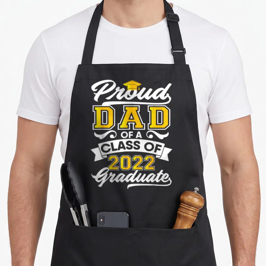 Proud class dad apron - Yellow and white Proud Dad Class of 2022 Graduate text with cap and banner — shown on a black cotton canvas apron against a white background