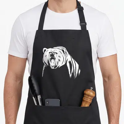 Grizzly outdoor bear apron - White line-art illustration of a roaring bear head and shoulders centered on black fabric — shown on a black cotton canvas apron against a white background