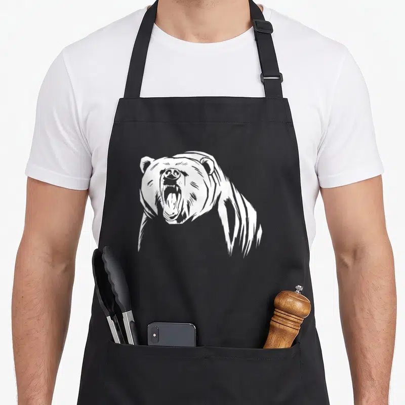 Grizzly outdoor bear apron - White line-art illustration of a roaring bear head and shoulders centered on black fabric — shown on a black cotton canvas apron against a white background