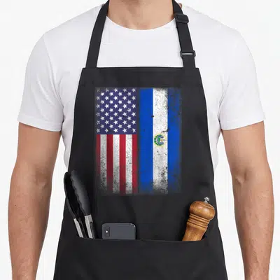 Salvadorean salvadoran apron - Distressed US and El Salvador flags side by side in blue white and red — shown on a black cotton canvas apron against a white background