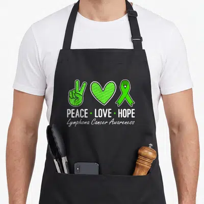 Hope ribbon apron - Green peace hand, striped heart, and ribbon with white text PEACE LOVE HOPE Lymphoma Cancer — shown on a black cotton canvas apron against a white background
