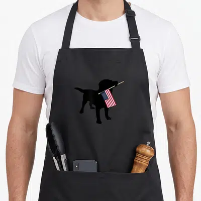 Holding 4th of july apron - Black dog silhouette holding red white and blue flag in mouth — shown on a black cotton canvas apron against a white background