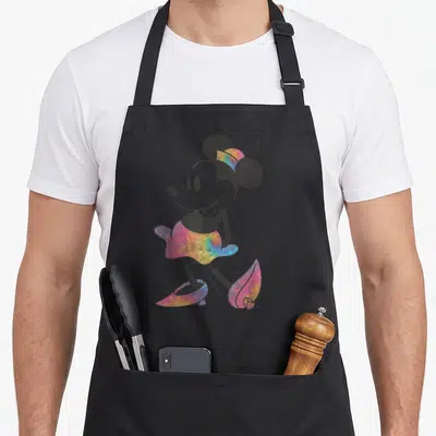 Friend tie apron - Cartoon Minnie Mouse wearing tie-dye skirt shoes and headband in pink yellow blue purple — shown on a black cotton canvas apron against a white background