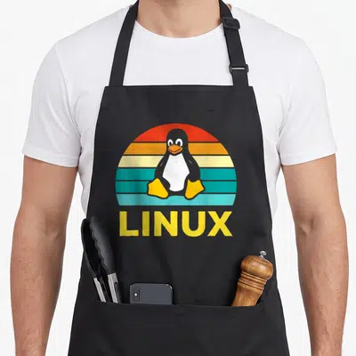 Penguin nerd apron - Retro penguin centered before striped sun with LINUX text below in yellow — shown on a black cotton canvas apron against a white background