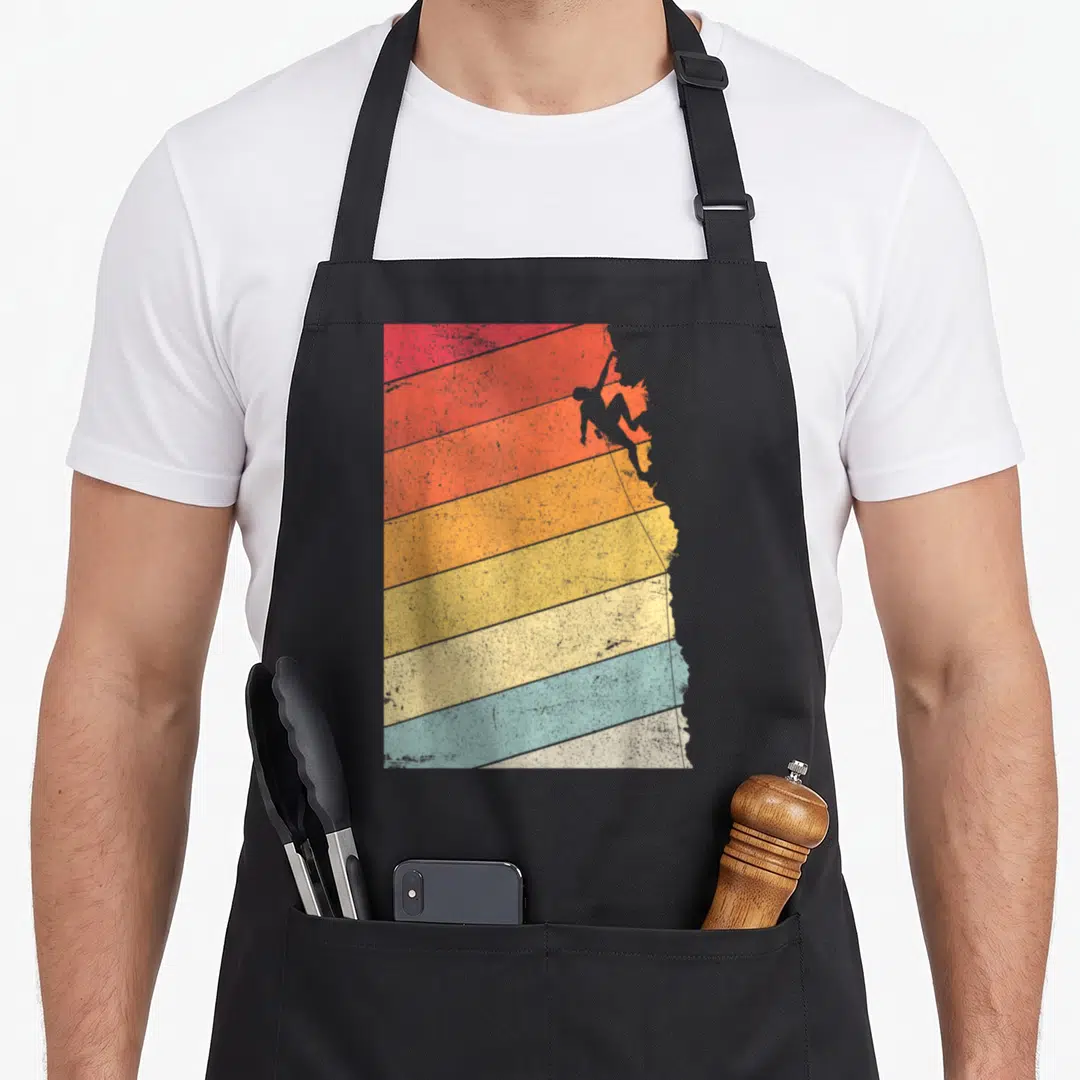 Rock climbing bouldering addict apron - Grey climber silhouette on diagonal red orange yellow beige blue and grey — shown on a black cotton canvas apron against a white background
