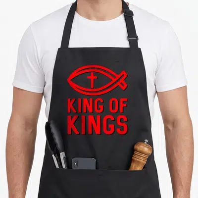 Fish king of the grill apron - Red ichthys fish symbol with internal cross above stacked KING OF KINGS text — shown on a black cotton canvas apron against a white background