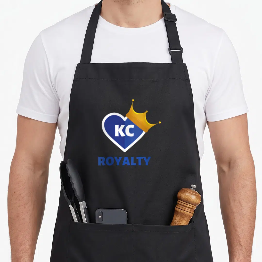 Blue crown royal apron - Blue heart with white border containing KC text, topped with a gold crown, and ROYALTY printed — shown on a black cotton canvas apron against a white background