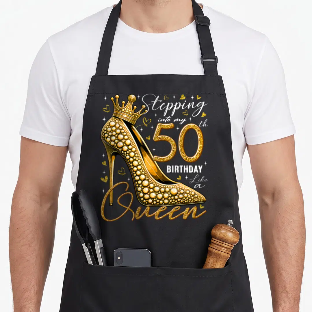 Heel stepping birthday apron - Gold glitter high heel with crown and 50th birthday quote on black apron — shown on a black cotton canvas apron against a white background