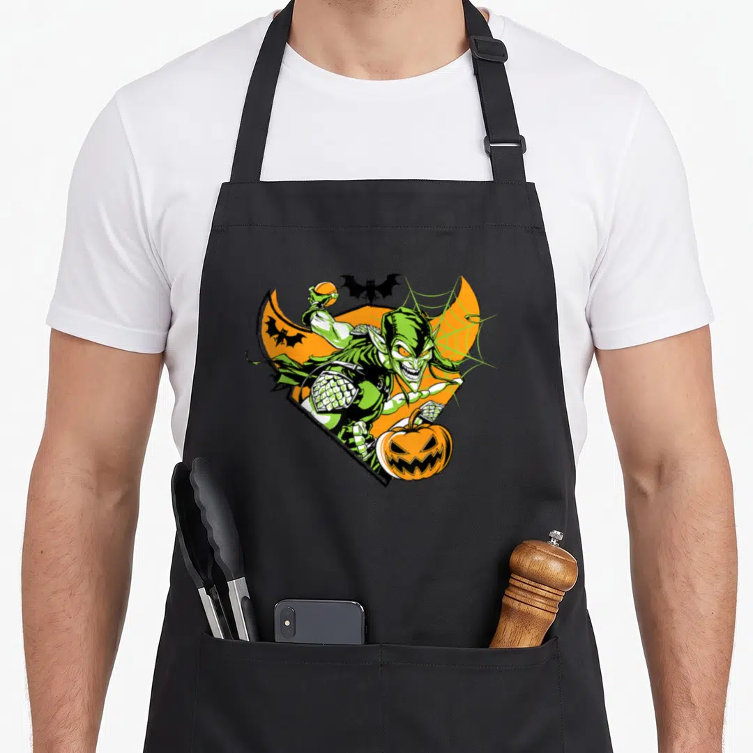 Bomb halloween apron - Green goblin cartoon character holding pumpkin with bats and orange crescent background — shown on a black cotton canvas apron against a white background