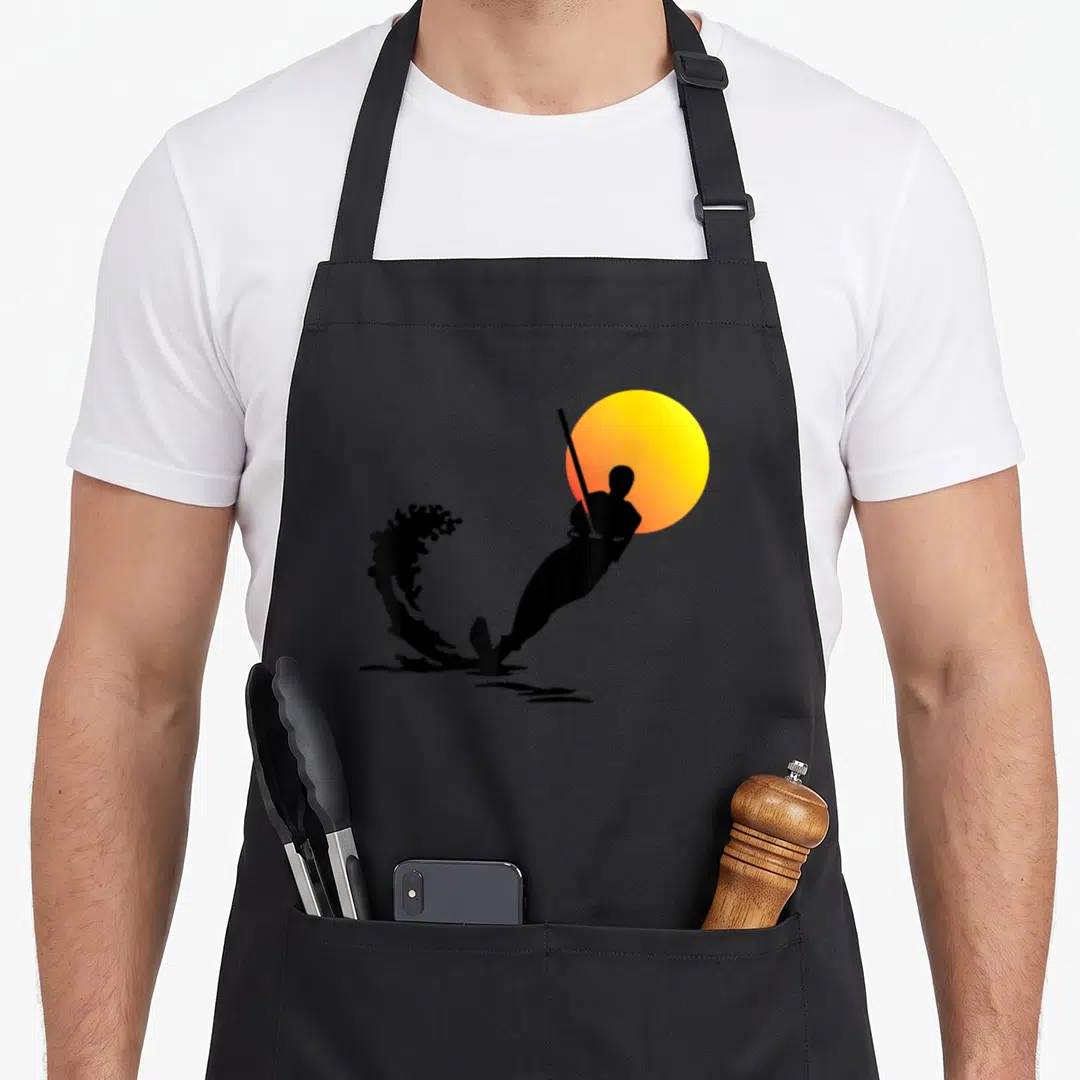 Water skiing apron - Black golfer silhouette swinging against yellow-orange sun with water splash — shown on a black cotton canvas apron against a white background