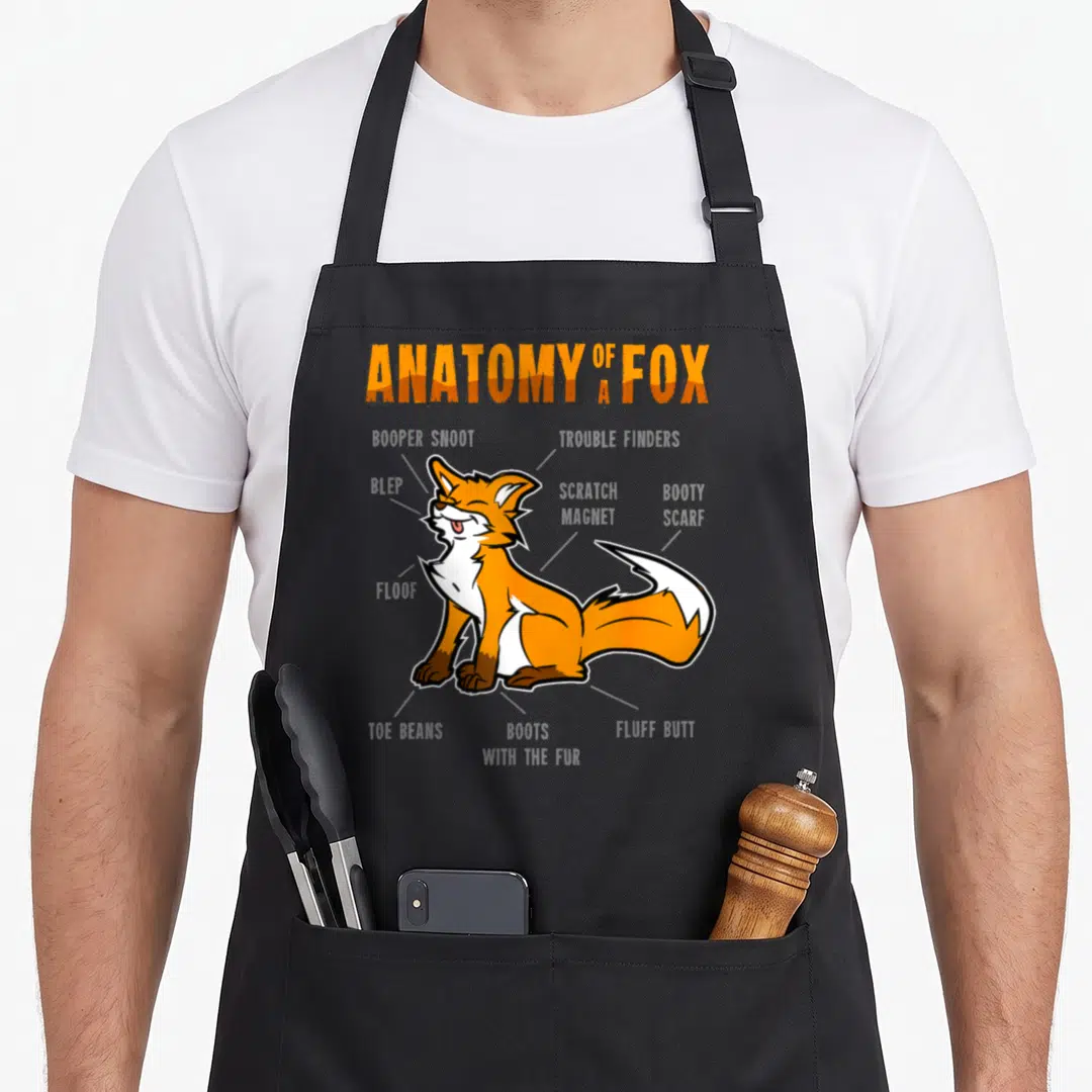 Fursona anatomy apron - Cartoon fox diagram labeled with terms like Blep, Toe Beans, and Floof in orange and grey — shown on a black cotton canvas apron against a white background