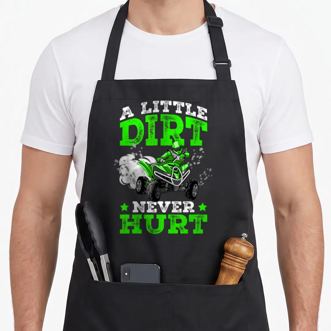 Dirt atv apron - Green ATV rider illustration with A Little Dirt Never Hurt text and white dust cloud — shown on a black cotton canvas apron against a white background