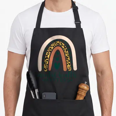 Mental leopard aprons - Rainbow with four arcs, three stacked hearts, mental health MATTERS text in beige green yellow — shown on a black cotton canvas apron against a white background